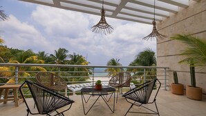 A balcony with wicker chairs, a small table, and potted plants. - Amazing Beachfront Villa (San Miguel de Cozumel)