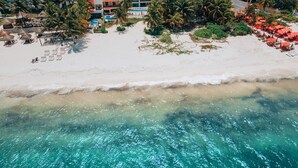 An aerial view of a beach with a hotel complex, including multiple buildings, palm trees, and a clear blue sea. - Amazing Beachfront Villa (San Miguel de Cozumel)