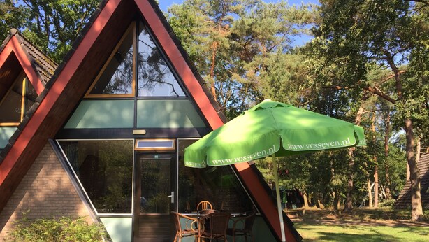 Un bâtiment moderne doté d’un toit triangulaire, d’une entrée avec une porte en verre et d’un grand parasol vert sur lequel figure l’adresse d’un site web.