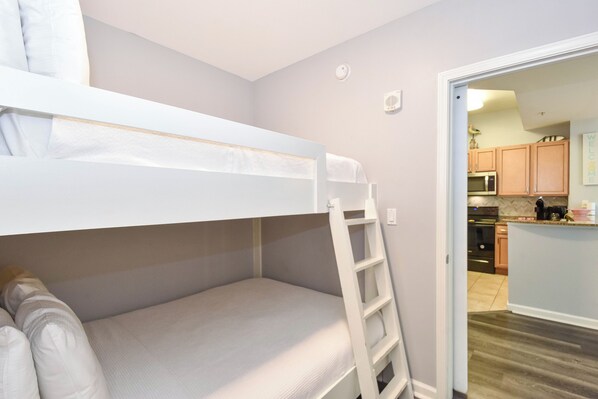 Una cama litera con escalera, una kitchenette y una puerta que da a otra habitación.
