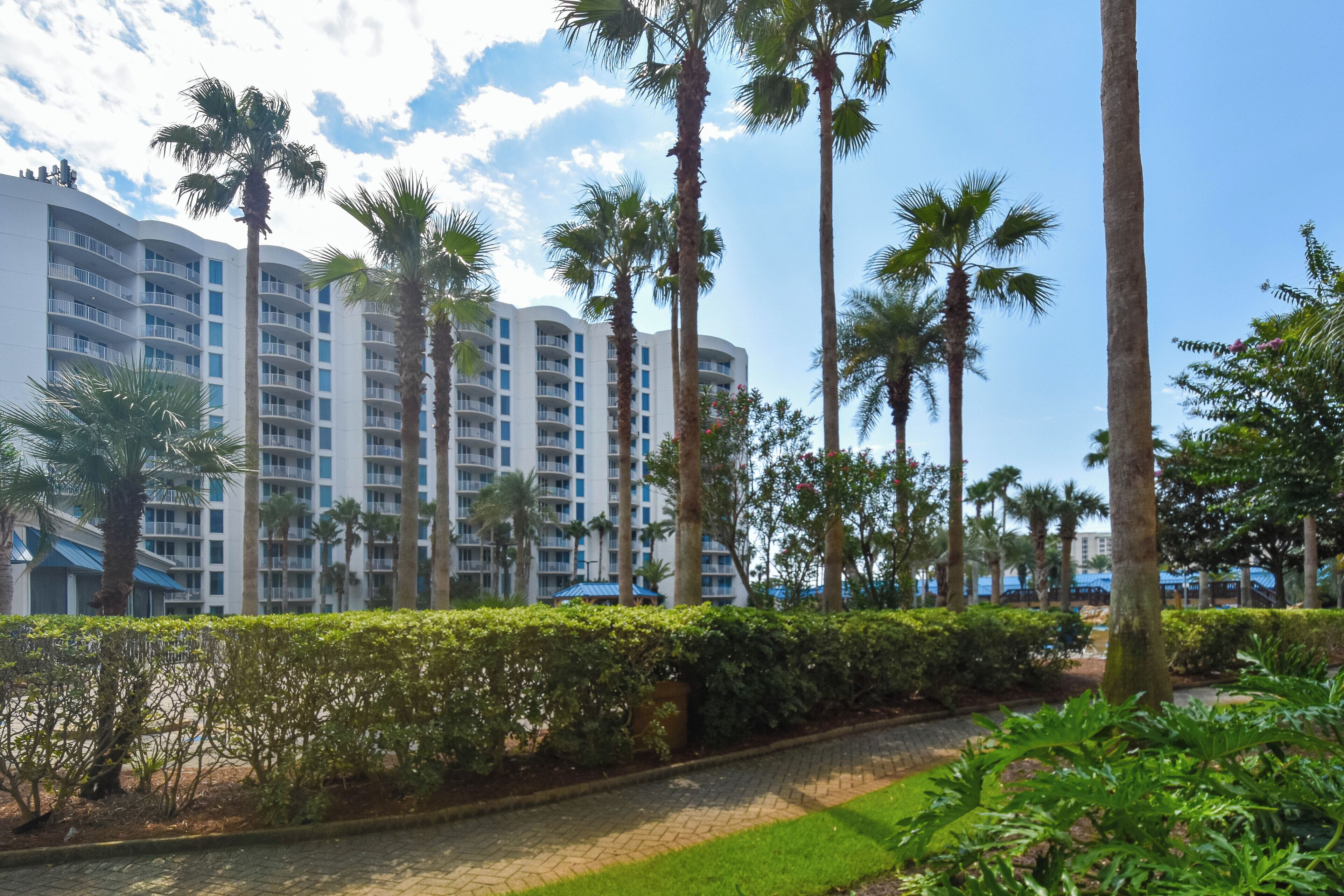A hotel with multiple floors, surrounded by palm trees and greenery.