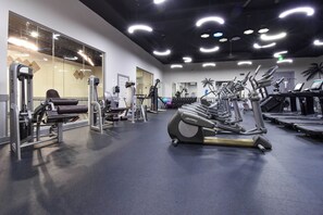 Une salle de sport équipée de matériel d’exercice, dotée d’un mur recouvert de miroirs et d’un plafond orné de luminaires circulaires.