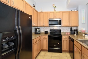 A kitchen with wooden cabinets, a black refrigerator, a microwave, a stove, and a coffee maker.