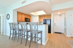 A modern kitchen with wooden cabinets, a microwave, a refrigerator, and a bar area with stools. - Calming Condo w/ XL Balcony & Lagoon Pool at The Palms of Destin! ππ β (Destin)
