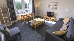 Ett modernt vardagsrum med en soffa, ett soffbord, ett TV-bord och en matplats med ett bord och stolar.