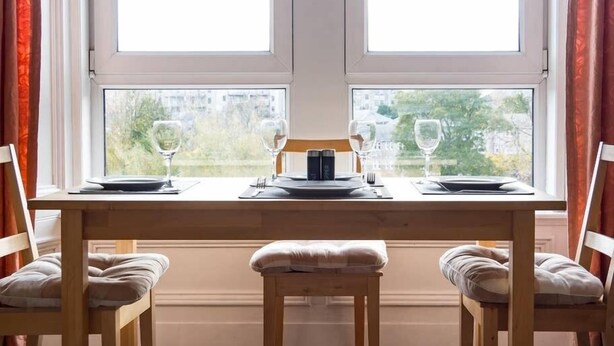Ett bord dukat för två personer med utsikt över byggnader genom stora fönster.