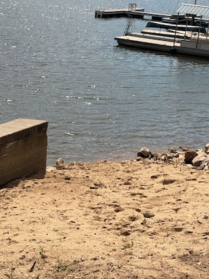 Une plage de sable avec une structure en béton, un quai avec des bateaux et une eau calme.