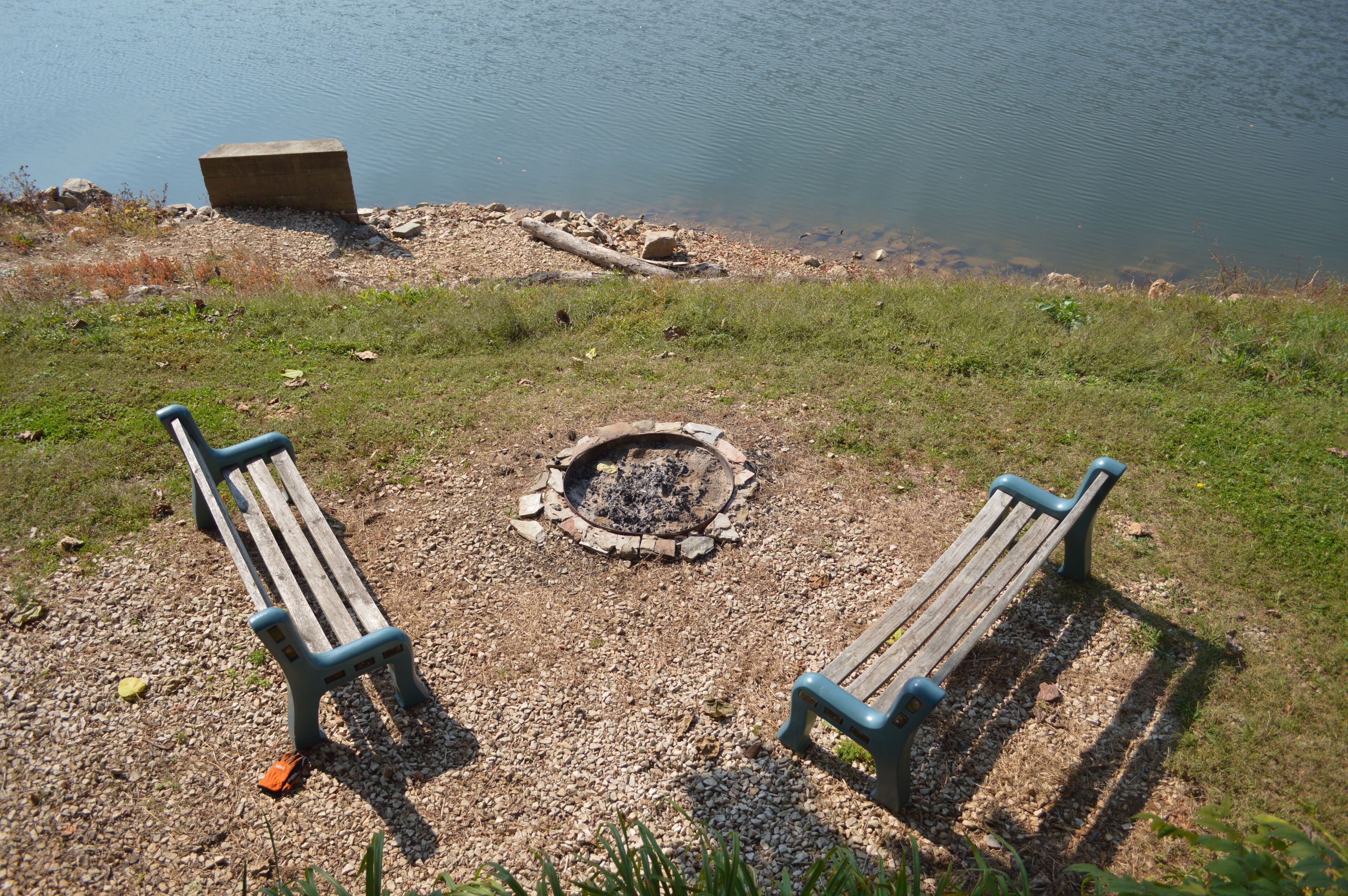 A lakeside setting with two wooden benches facing a fire pit.