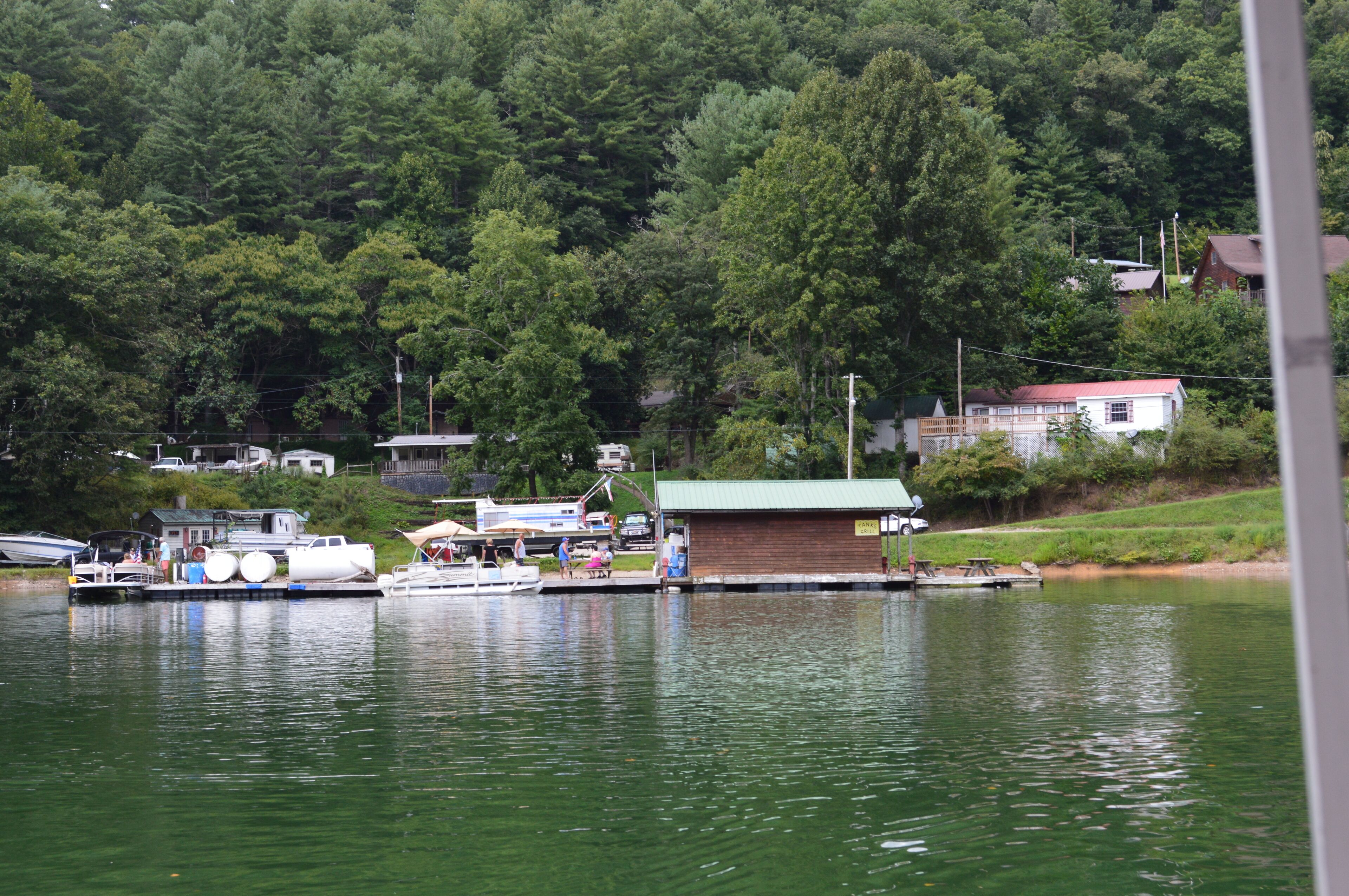 Un quai avec des bateaux, un petit bâtiment doté d’un toit végétalisé et, au loin, une colline boisée.