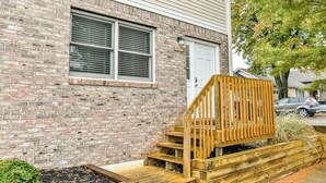 A brick building with a white door, a window with blinds, and a wooden staircase leading to a deck. - Roomy 3 BR Condo Walkable to IU (Bloomington)