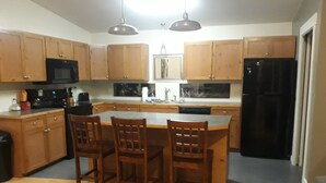 A kitchen with wooden cabinets, a black refrigerator, a microwave, and a dining area with two chairs. - Serene Lake Home (Fort Scott)