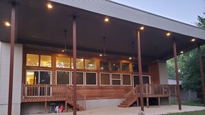 A two-story building with a covered patio area, large windows, and a wooden deck with stairs. - Serene Lake Home (Fort Scott)