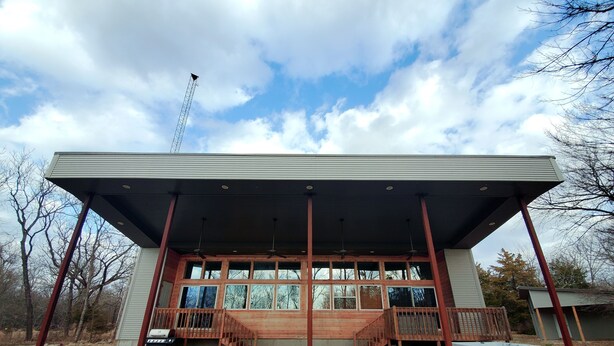 A modern building with a covered patio, large windows, and a wooden deck. - Serene Lake Home (Fort Scott)