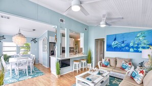 A spacious living area with a dining table, white chairs, a sofa, and a coffee table. There is a ceiling fan, a chandelier, and a large painting of fish on the wall. - ATLANTIS...Ocean Front Cottage Retreat! (Cudjoe Key)