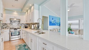 A modern kitchen with white cabinets, a stainless steel stove, and a large island with a sink. - ATLANTIS...Ocean Front Cottage Retreat! (Cudjoe Key)