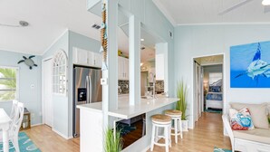 A modern kitchen with white cabinetry, a stainless steel refrigerator, and a central island with bar stools. - ATLANTIS...Ocean Front Cottage Retreat! (Cudjoe Key)