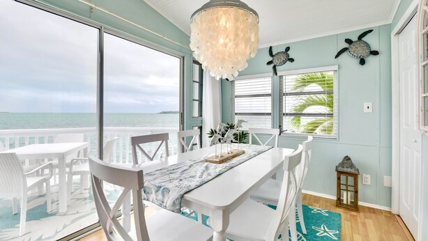 A dining area with a view of the ocean, a chandelier, and a table set with white chairs. - ATLANTIS...Ocean Front Cottage Retreat! (Cudjoe Key)