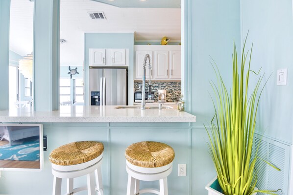 A modern kitchen with white cabinets, a stainless steel refrigerator, and a large green plant. - ATLANTIS...Ocean Front Cottage Retreat! (Cudjoe Key)