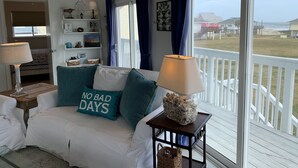 Un dormitorio con cama, mesita de noche, lámpara, ventana con cortinas y vista a la playa.