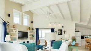 Amplia sala de estar con un sofá, una mesa de centro y un televisor. Se observa una cocina al fondo.
