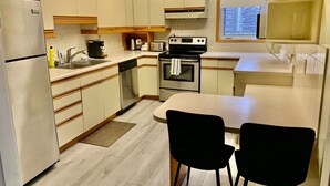 A compact kitchen with a refrigerator, dishwasher, oven, and a small dining area with two chairs.