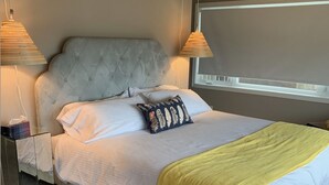 A neatly made bed with a tufted headboard, white linens, and a yellow throw blanket. There are two bedside lamps and a small bedside table with a tissue box.