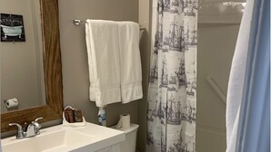 A bathroom with a white sink, vanity, and toilet. There is a towel hanging on the wall and a shower curtain with a nautical print.