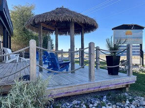 Eine Holzterrasse mit blauen Stühlen und einem Gazebo mit Reetdach.