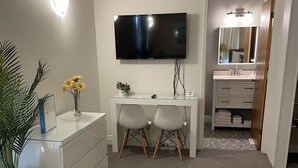Ein modernes Badezimmer mit einem weißen Waschtisch, einem großen Spiegel und einem flachbildschirmfernseher, der über dem Waschtisch angebracht ist.