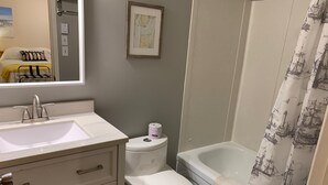 Ein Badezimmer mit einem weißen Waschbecken, einer Toilette und einer Badewanne. An der Wand hängt eine gerahmte Karte und ein Duschvorhang mit einem Meeresmotiv.