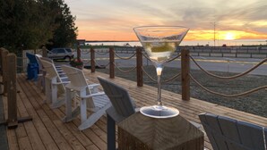 A sunset view from a wooden deck with a glass of white wine, lounge chairs, and a fence. - 202 - Executive Rm Lake View- Balcony 2 DBL (Port Elgin)