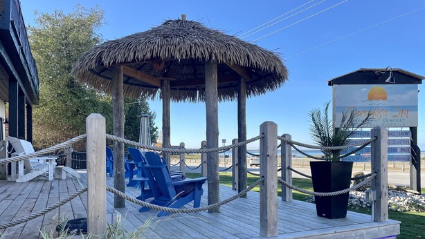 A wooden deck with blue chairs and a thatched-roof gazebo. - 202 - Executive Rm Lake View- Balcony 2 DBL (Port Elgin)