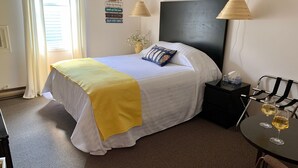 A hotel room with a bed, bedside table, lamp, and a table with glasses of wine.