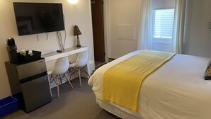 A hotel room with a bed, a desk with a chair, a television, and an air conditioning unit.