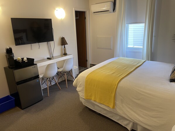 A hotel room with a bed, a desk with a chair, a television, and an air conditioning unit.