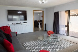 A modern living room with a flat-screen TV, a glass coffee table, and a sofa with red cushions.