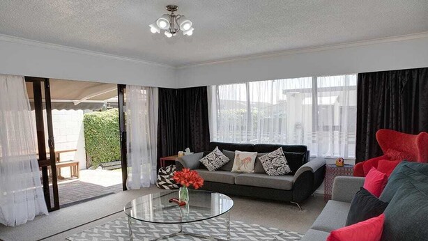 A modern living room with a glass coffee table, grey sofa, and red cushions.