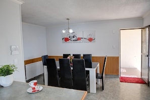 A dining area with a table and chairs, a potted plant, and a wall-mounted artwork.