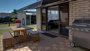 A patio with a barbecue grill, a wooden table, and a covered seating area.