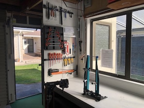 A workshop with tools and equipment, a window with a view of a house, and a door leading outside.