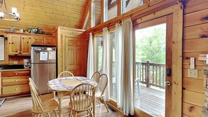 A wooden cabin with a dining area, kitchen, and a deck with a view of the outdoors. - Trail's End by Jackson Mountain Rentals (Gatlinburg)
