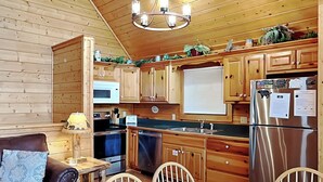 A cozy kitchen with wooden cabinets, a stainless steel refrigerator, a microwave, and a sink. There is a dining table with chairs and a couch with a patterned cushion. - Trail's End by Jackson Mountain Rentals (Gatlinburg)
