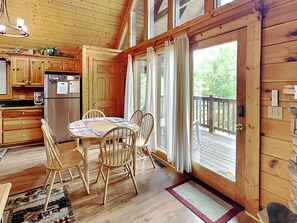 Una cabaña de madera con comedor, cocina y una terraza con vistas al exterior.