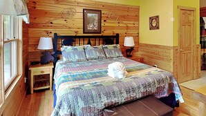 A wooden-paneled bedroom with a bed, two bedside tables, a nightstand, a window, and a door. - Trail's End by Jackson Mountain Rentals (Gatlinburg)