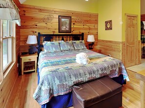 A wooden-paneled bedroom with a bed, two bedside tables, a nightstand, a window, and a door. - Trail's End by Jackson Mountain Rentals (Gatlinburg)