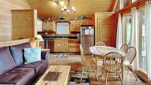 Een gezellig interieur van een blokhut met een houten eettafel, stoelen, een bank en een keuken met houten kastjes en een koelkast.