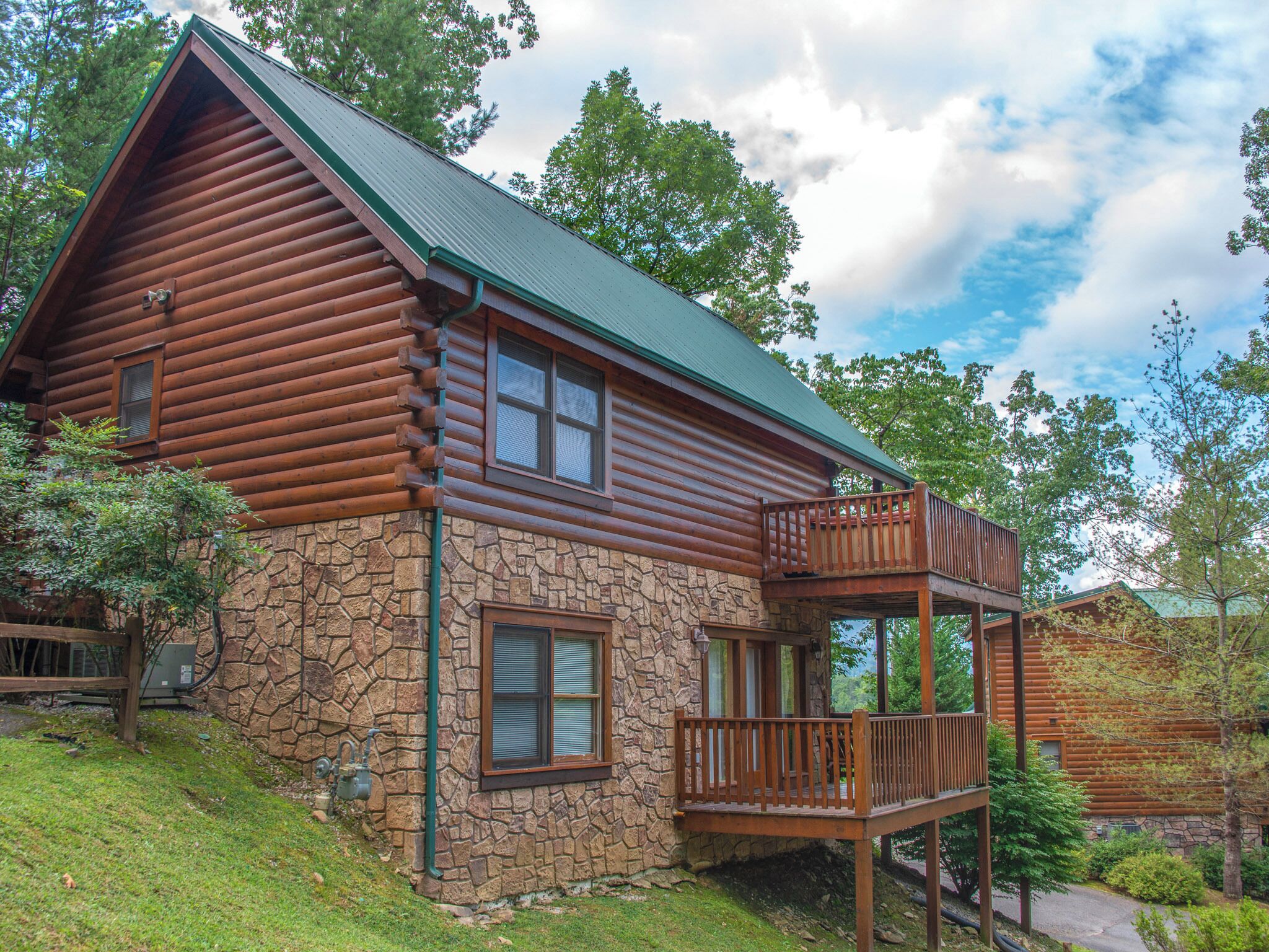 A log cabin with a stone foundation, a green roof, and a wooden balcony.