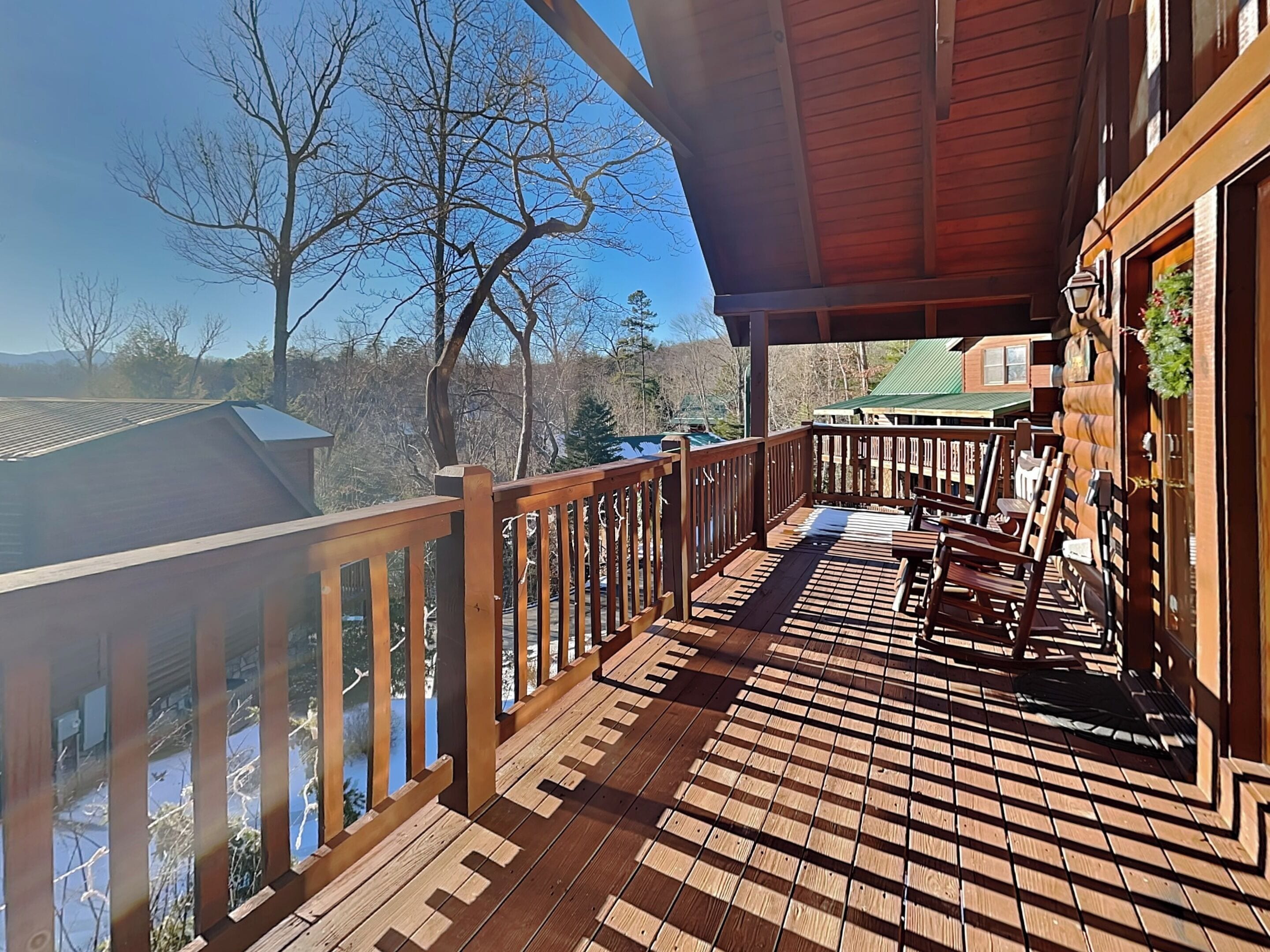 A wooden deck with a railing, a bench, and a view of trees and buildings in the background.