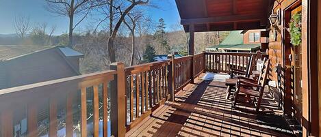 A wooden deck with a railing, a bench, and a view of trees and buildings in the background.