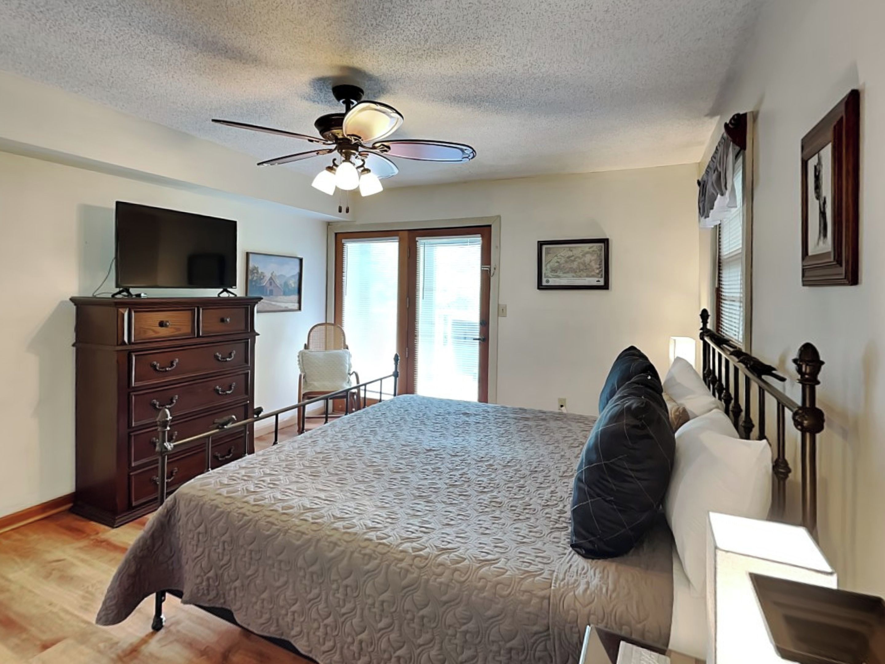 A bedroom with a bed, dresser, ceiling fan, and a television.